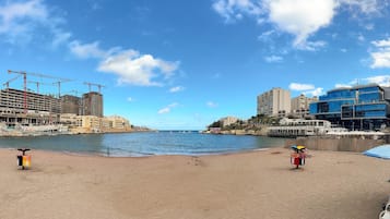 A beach with a sandy shore, a few umbrellas, and a building under construction in the background.