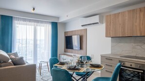 Un saló modern amb un sofà, una taula de menjador preparada per a dues persones i una cuina amb armaris de fusta i forn integrat.