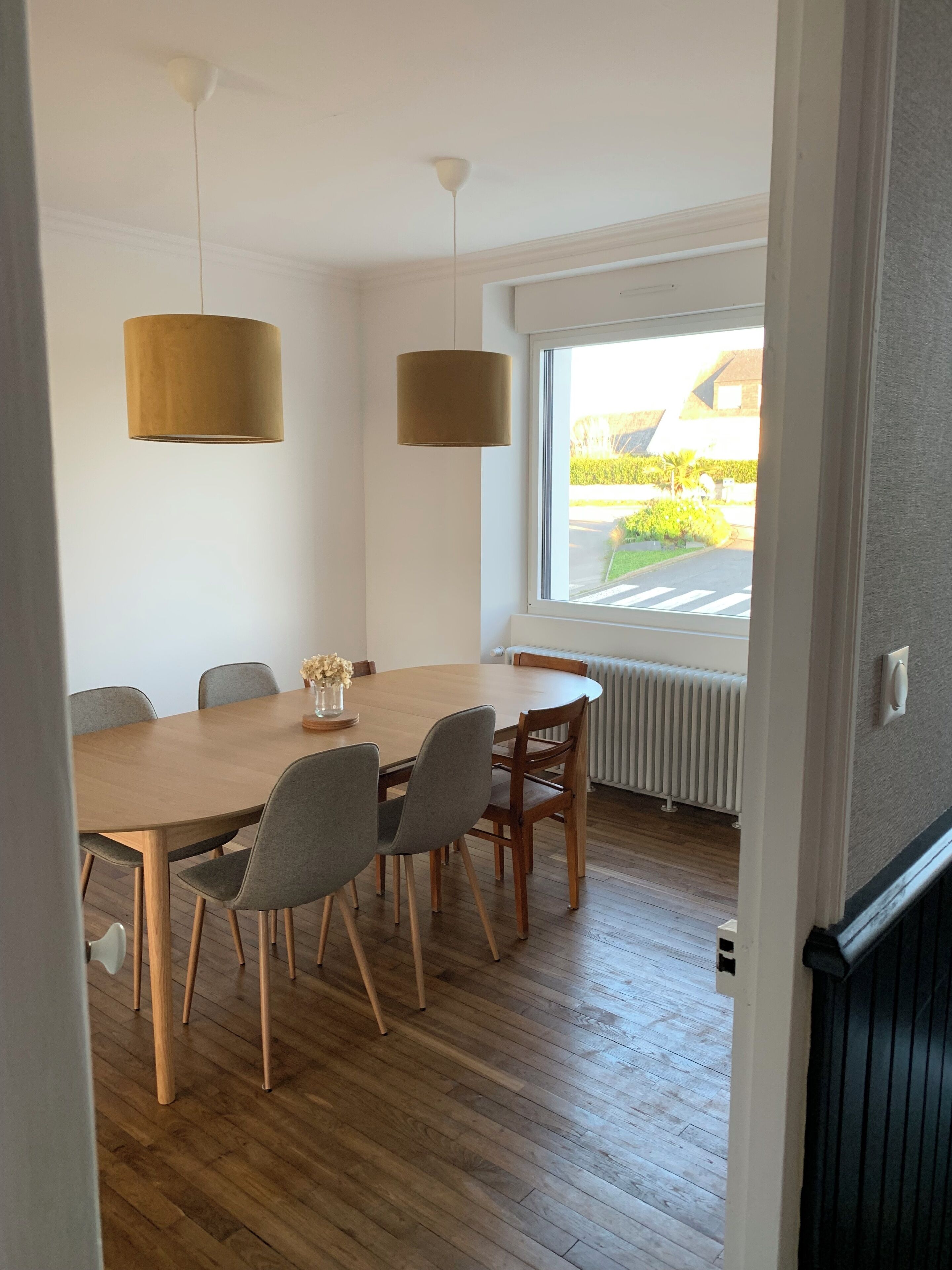 A dining area with a wooden table, grey chairs, and two hanging lamps.