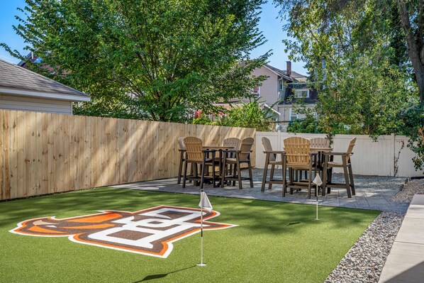 A backyard with a wooden fence, a grassy area with a logo, and outdoor furniture.