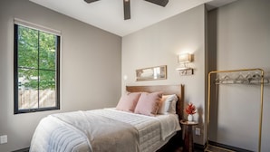 Un dormitorio con un ventanal grande, una cama con cabecera de madera, lámparas de noche y un perchero.