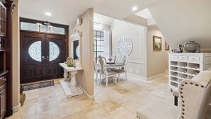 A spacious entryway with a dark wooden door, a white console table, and a dining area with a white table and chairs.