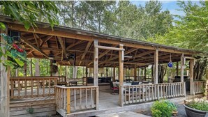 A covered outdoor area with wooden benches and tables, surrounded by trees.
