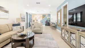 A modern living room with a sofa, coffee table, and a TV. - Luxury 6BR • Heated Pool Included • Theater •Disney • H2O Perks • No Resort Fees (Kissimmee)
