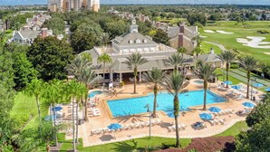 A resort with a large swimming pool, palm trees, and a golf course in the background. - Luxury 6BR • Heated Pool Included • Theater •Disney • H2O Perks • No Resort Fees (Kissimmee)