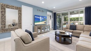 A living room with a TV, sofa, and a glass door leading to a balcony. - Luxury 6BR • Heated Pool Included • Theater •Disney • H2O Perks • No Resort Fees (Kissimmee)
