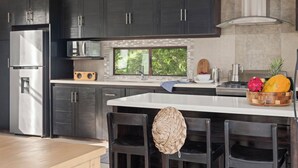 A modern kitchen with dark cabinetry, a stainless steel refrigerator, a microwave, and a large window. - Vista Popoyo 3BR Coastal Retreat with Surf & Mangrove Views (Las Salinas)