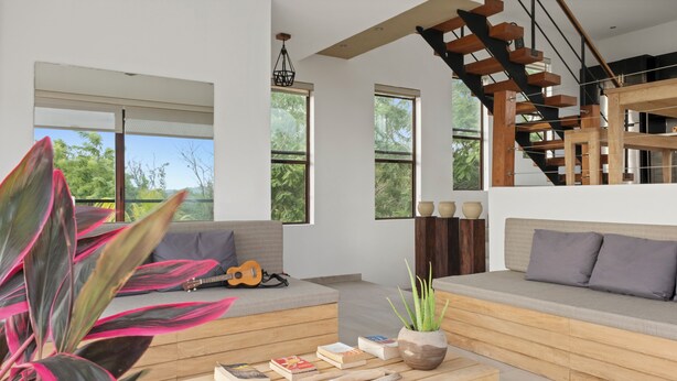 A modern living room with a wooden staircase, large windows, and a plant. - Vista Popoyo 3BR Coastal Retreat with Surf & Mangrove Views (Las Salinas)