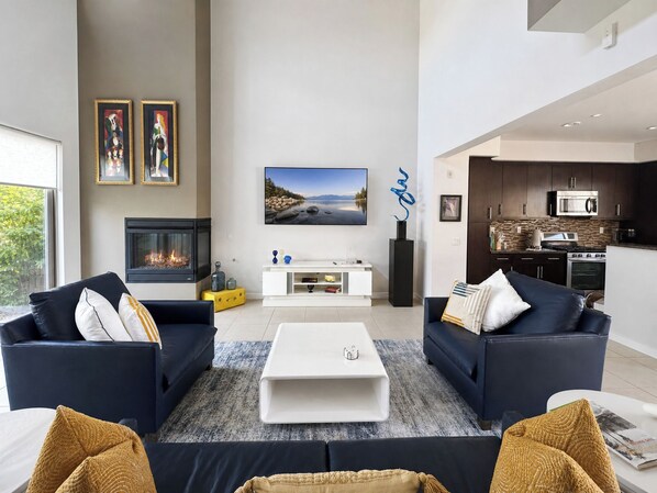 A modern living room with two sofas, a coffee table, a fireplace, and a large TV.