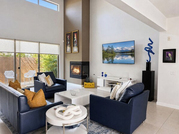 A modern living room with a fireplace, two sofas, a coffee table, and a large window overlooking greenery.
