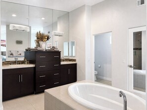 A modern bathroom with a large mirror, dark cabinetry, a white bathtub, and a shower area.