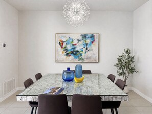 A dining area with a glass table, brown chairs, a blue vase, a yellow vase, and a potted plant.