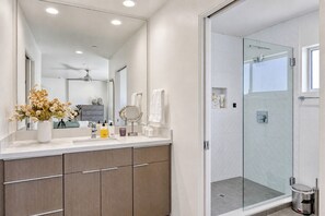 A modern bathroom with a glass shower enclosure, a vanity with a mirror, and a vase of flowers on the counter.