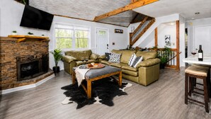Een ruime woonkamer met een open haard, leren banken, een eethoek en een trap.