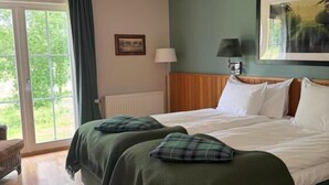 Ein Hotelzimmer mit einem großen Bett, einem Holzkopfende, einem Fenster mit Vorhängen, einer Lampe und einem Bild an der Wand.