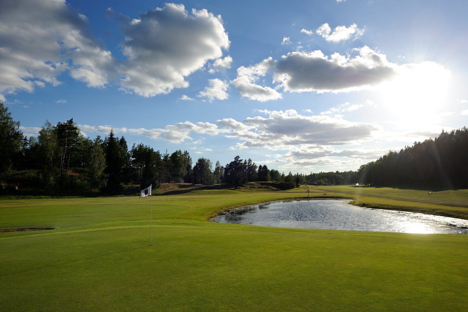 En golfbana med flaggstång, vattenhinder och träd.