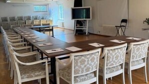 Ein Konferenzraum mit einem langen Tisch, weißen Stühlen, einem Fernseher und einer Projektionsleinwand.