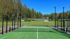 A tennis court with a net, surrounded by a fence, trees, and a clear sky. - Ada Krog Hotell & Konferens (Trosa)