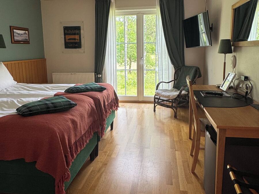 A hotel room with a bed, a desk, a chair, a television, and a window with curtains.