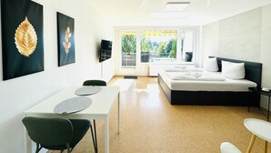 Camera d'albergo moderna con un letto, una scrivania e una sedia. Due opere d'arte alle pareti, una TV e una finestra con vista sul verde.