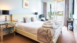 A hotel room with a large bed, a desk with a lamp, a chair, and a view of the outside. - Howells Mere 16, Indian Summer - Lakeside Cottage | Sleeps 4 in 2 bedrooms (Somerford Keynes)