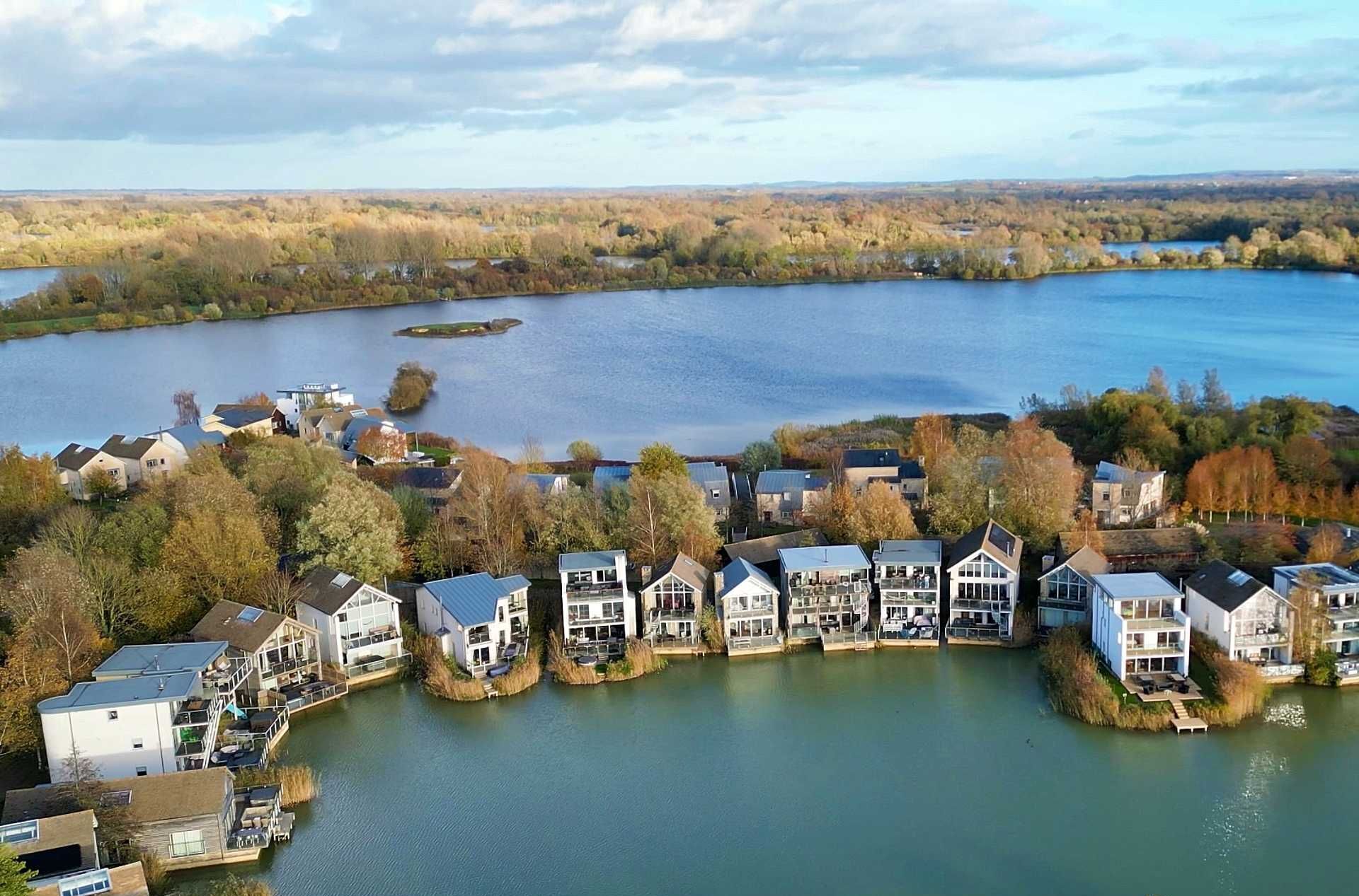 An aerial view of a lakeside residential area with houses along the water's edge, featuring a mix of modern and traditional architecture.