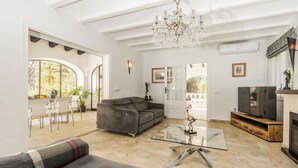 A spacious living room with a grey sofa, a glass coffee table, a TV on a wooden stand, and a chandelier. - Villa Tranquila (Denia)