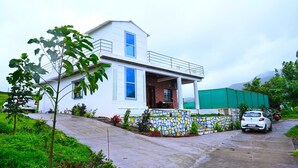 A two-story white house with a balcony, a stone wall with colorful tiles, and a green fence. - Pawna Ns4 villa (Mawal)
