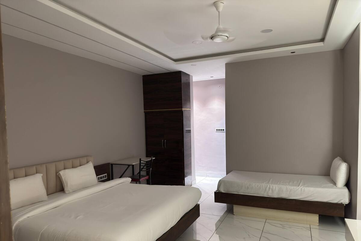 A modern bedroom with two beds, a dark wardrobe, and a ceiling fan.