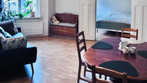 A cozy room with a wooden floor, a round dining table with chairs, a bench, and a window with plants. - Nordic Vintage Studio (Helsinki)