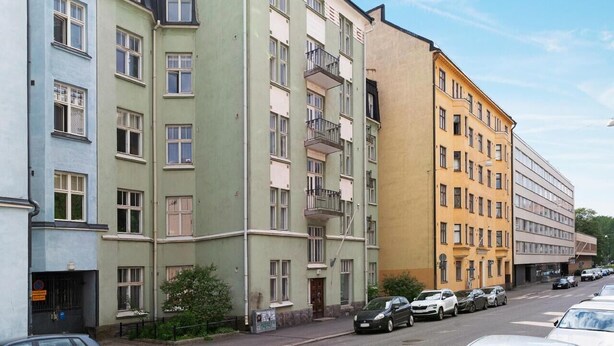 A row of multi-story residential buildings with balconies, parked cars, and a clear sky. - Nordic Vintage Studio (Helsinki)