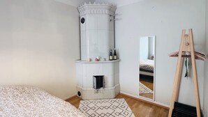 A bedroom with a large bed, a white fireplace, a mirror, and a wooden ladder. - Nordic Vintage Studio (Helsinki)