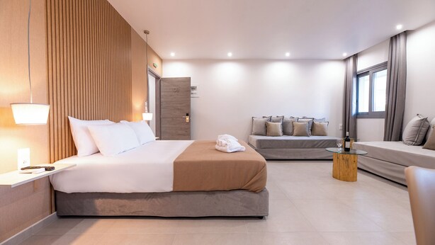 A modern hotel room with a large bed, a smaller sofa, a wooden coffee table, and a view of the city. - AIRSCAPE HOTEL FREE SHUTTLE ATH AIRPORT (Spata-Artemida)