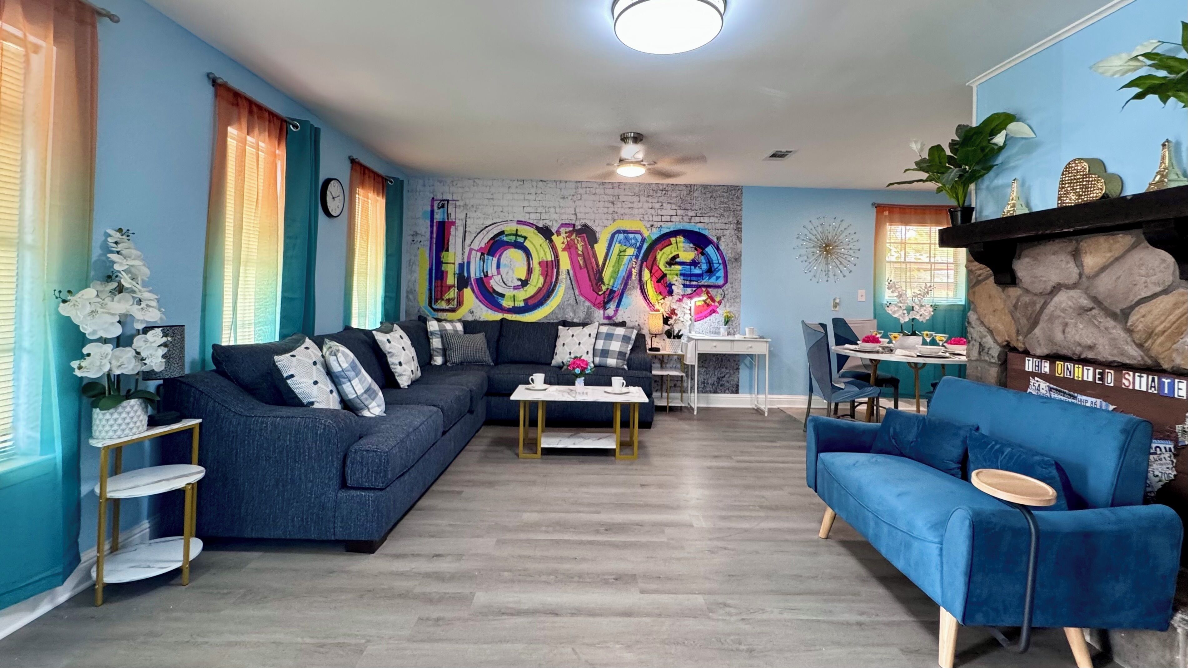 A modern living room with a sectional sofa, a blue armchair, and a coffee table. A colorful 'LOVE' mural adorns the wall.