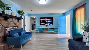 Un salon avec un canapé bleu, un mur en pierre, un téléviseur à écran plat et une porte dotée d’un cadre bleu.