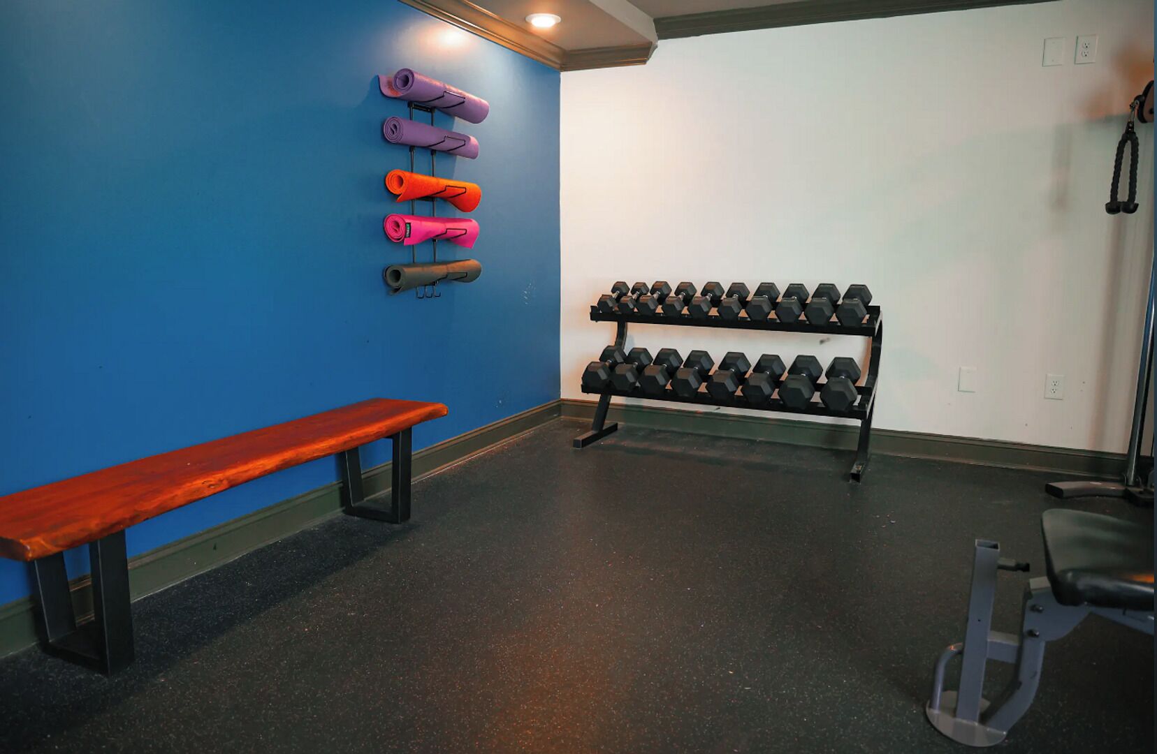 Une salle de sport équipée d’un banc, de tapis de yoga et d’un porte-haltères.