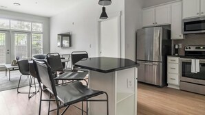 A modern kitchen with a central island, stainless steel appliances, and a dining area with chairs. - Landing | Amazing 2BD, Rooftop Lounge, Pool (Cary)