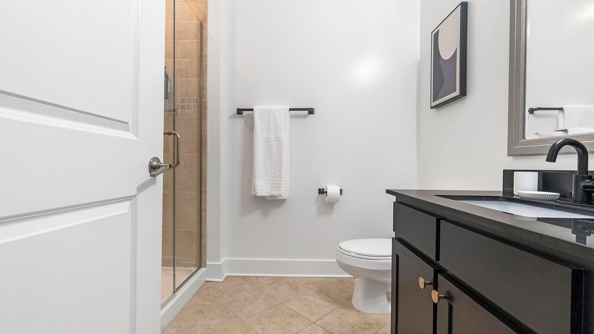 Ein modernes Badezimmer mit einer Duschkabine aus Glas, einer Toilette, einem Waschbecken mit schwarzer Arbeitsplatte und einem weißen Handtuch an einer Handtuchstange.