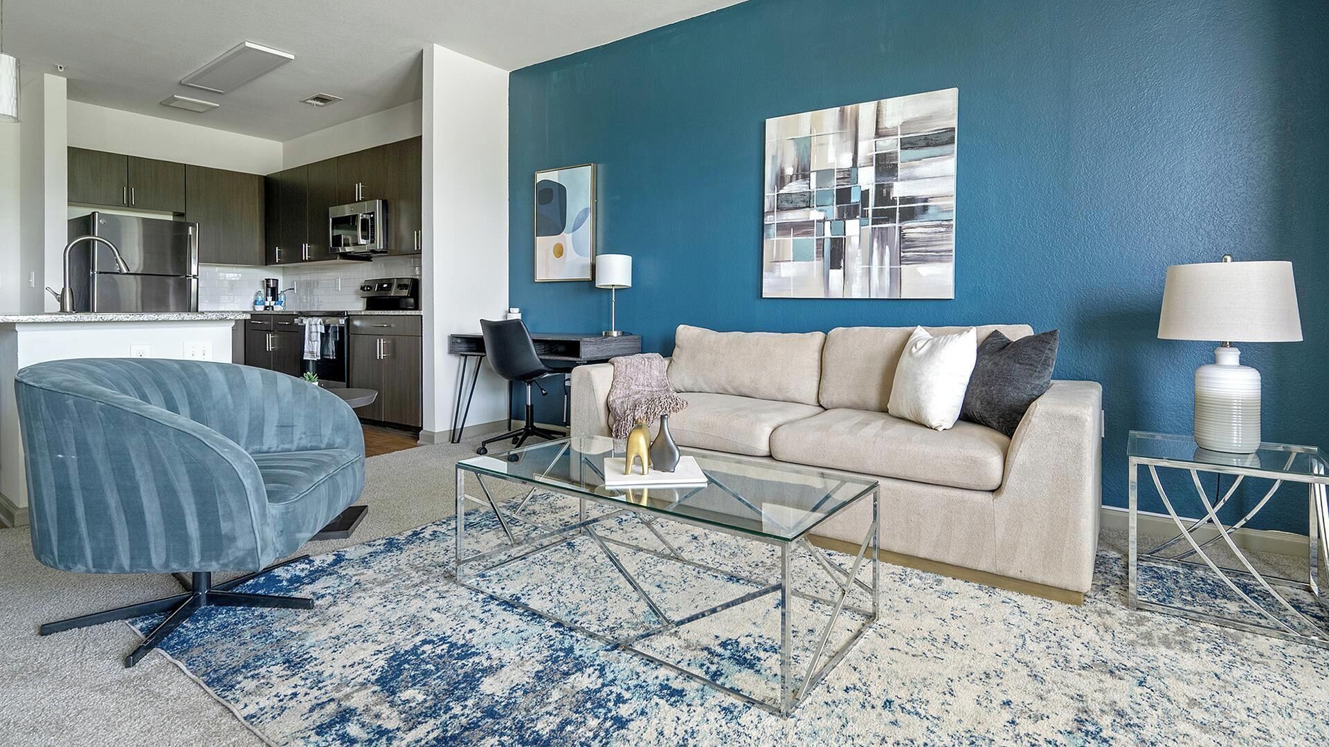 Ein modernes Wohnzimmer mit einem Glastisch, einem beigefarbenen Sofa und einer blauen Akzentwand.