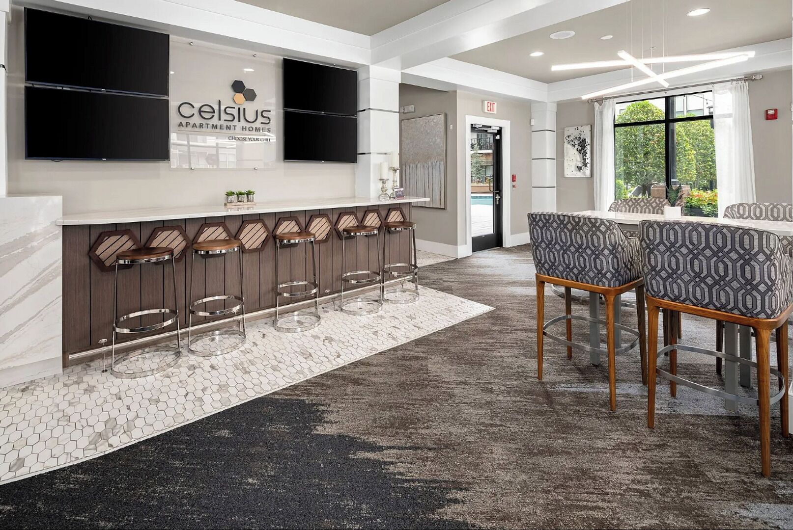 Zona de bar moderna con barra, taburetes y un área de estar con sillas estampadas.