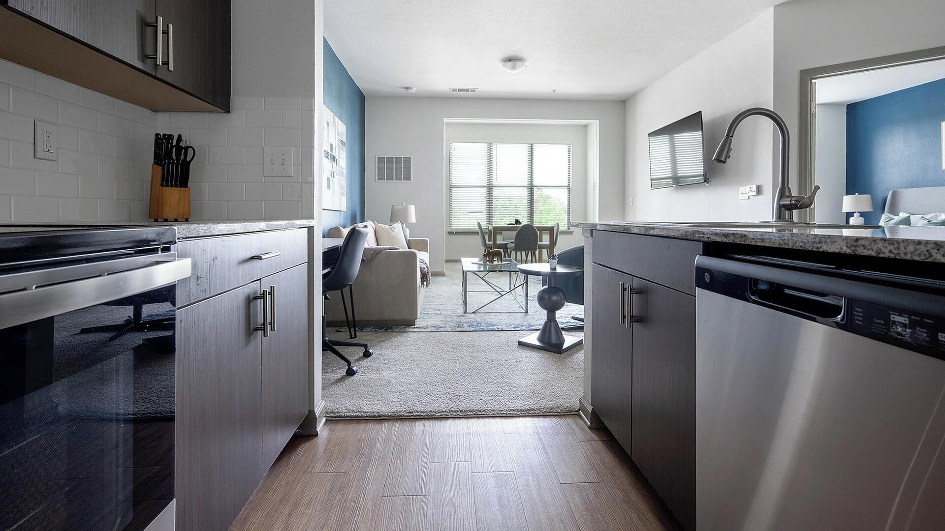 A modern kitchen with stainless steel appliances, a dining area with a table and chairs, and a view of the outdoors through large windows.
