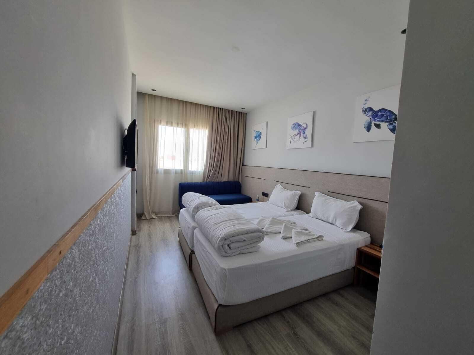 A hotel room with a large bed, a blue chair, and a window with curtains.