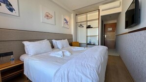 A hotel room with a large bed, a bedside table with a bottle, a TV mounted on the wall, and artwork on the walls. - Seashell (Oualidia)