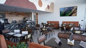 A restaurant with marble-topped tables and brown leather chairs, a bar area, and a mountain landscape painting on the wall. - Seashell (Oualidia)