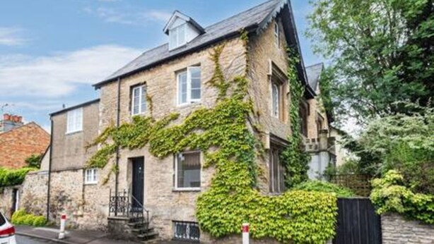 Ein Haus aus Stein mit Efeu an den Wänden, eine gut erkennbare Haustür und ein kleiner Vorgarten.