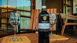Una botella de vino Brunello di Montalcino 2020 sobre una mesa de madera con dos copas de vino.