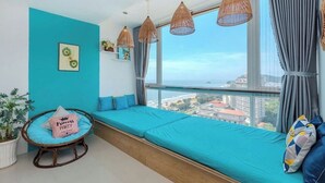 Una stanza con un'ampia finestra, un letto con biancheria azzurra, lampade pendenti in vimini e vista sulla città.