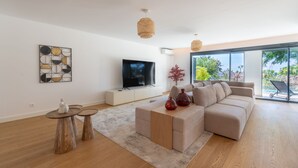 Una sala moderna con un televisor de pantalla plana grande, un sofá modular beige, una mesa de centro y un ventanal con vistas al exterior.