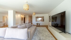 Una sala de estar moderna con un televisor de pantalla plana grande, un sofá seccional color beige y un ventanal que proporciona luz natural.