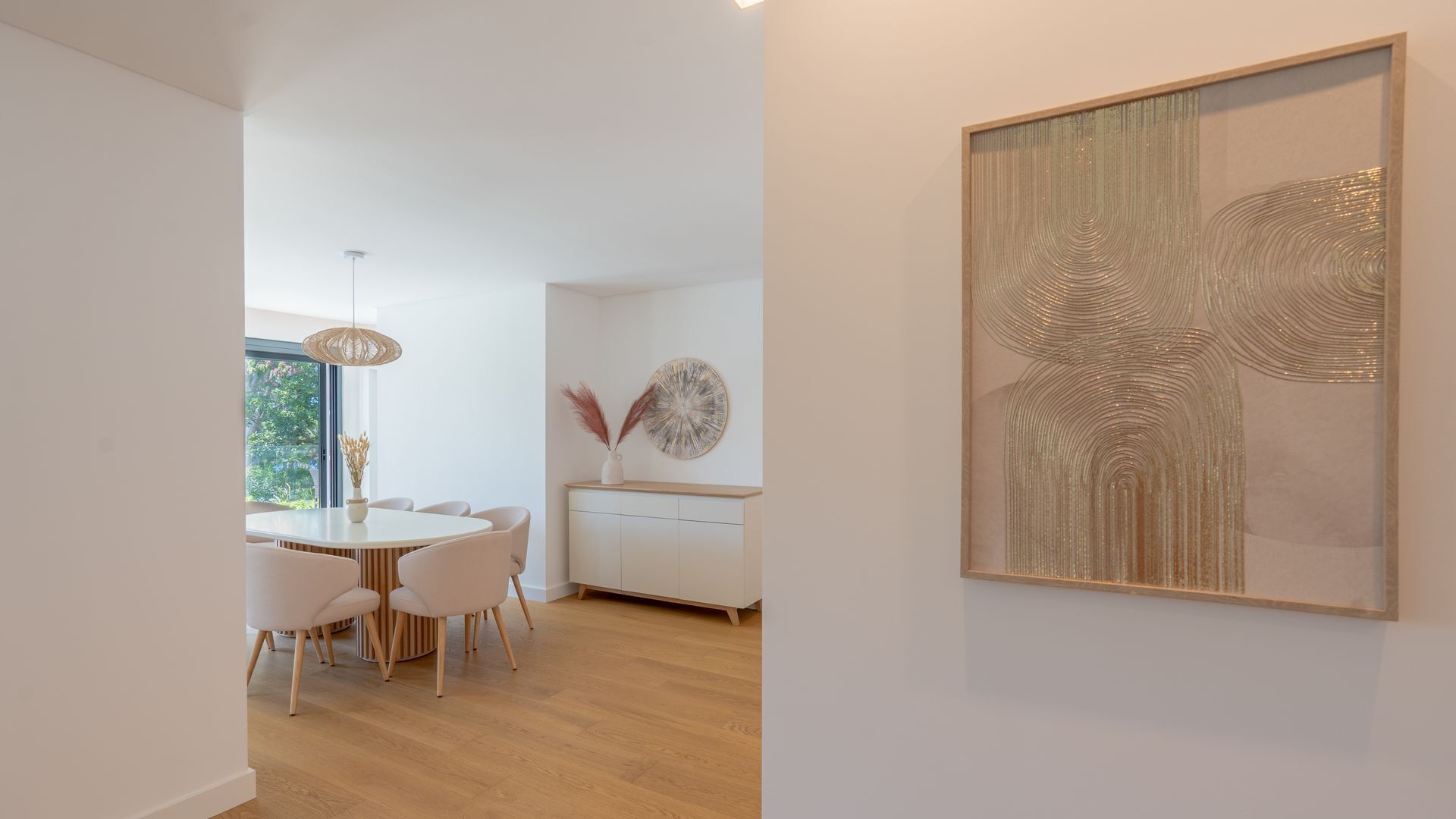 Un espace repas moderne avec une table ronde et des chaises, un meuble blanc et un grand tableau abstrait accroché au mur.